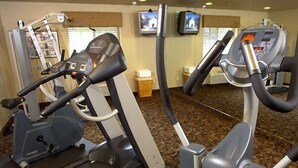 A gym with cardio machines, a television, and a window with blinds. - Crivitz Lodge (Crivitz)