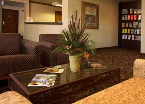 A lobby with patterned furniture, a glass coffee table with brochures, and a plant centerpiece. - Crivitz Lodge (Crivitz)