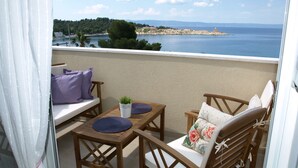 Un balcón con mobiliario de madera, una pequeña mesa y vista al mar y al paisaje distante.