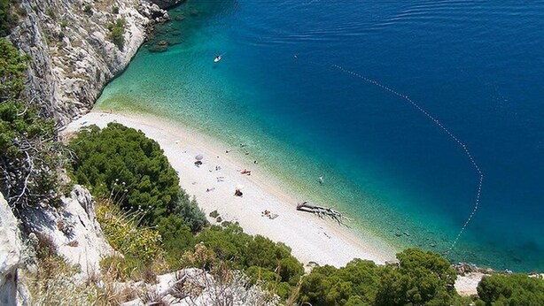 Una playa costera con aguas turquesas cristalinas, acantilados rocosos y vegetación densa.