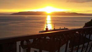 Vista al atardecer desde un balcón con vistas a una masa de agua y una tierra distante.