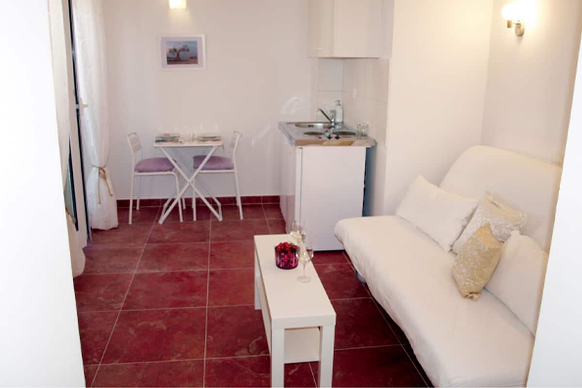 Un espace de vie compact comprenant un canapé blanc, une petite table, un coin repas avec une chaise et un coin cuisine.