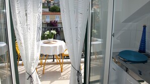 Un balcón con una mesa, cortinas blancas y vistas a edificios y montañas.