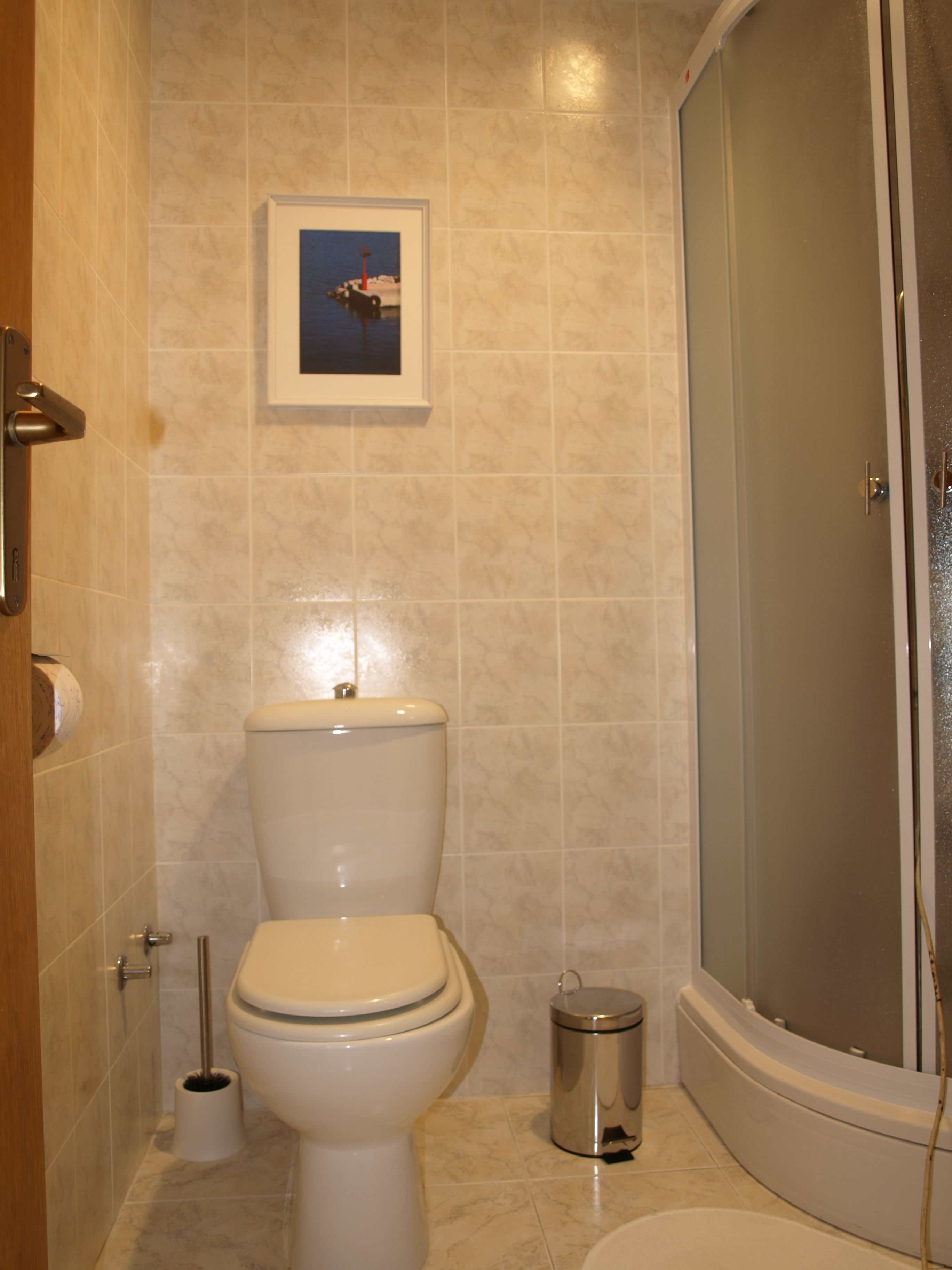 A bathroom with a toilet, a bidet, a trash bin, and a framed picture on the wall.