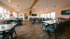 A spacious dining area with wooden tables and chairs, large windows, and hanging pendant lights. - Hotel Vos (Rangarthing ytra)