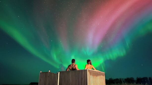 Two people in a wooden structure under a night sky with aurora borealis. - Hotel Vos (Rangarthing ytra)