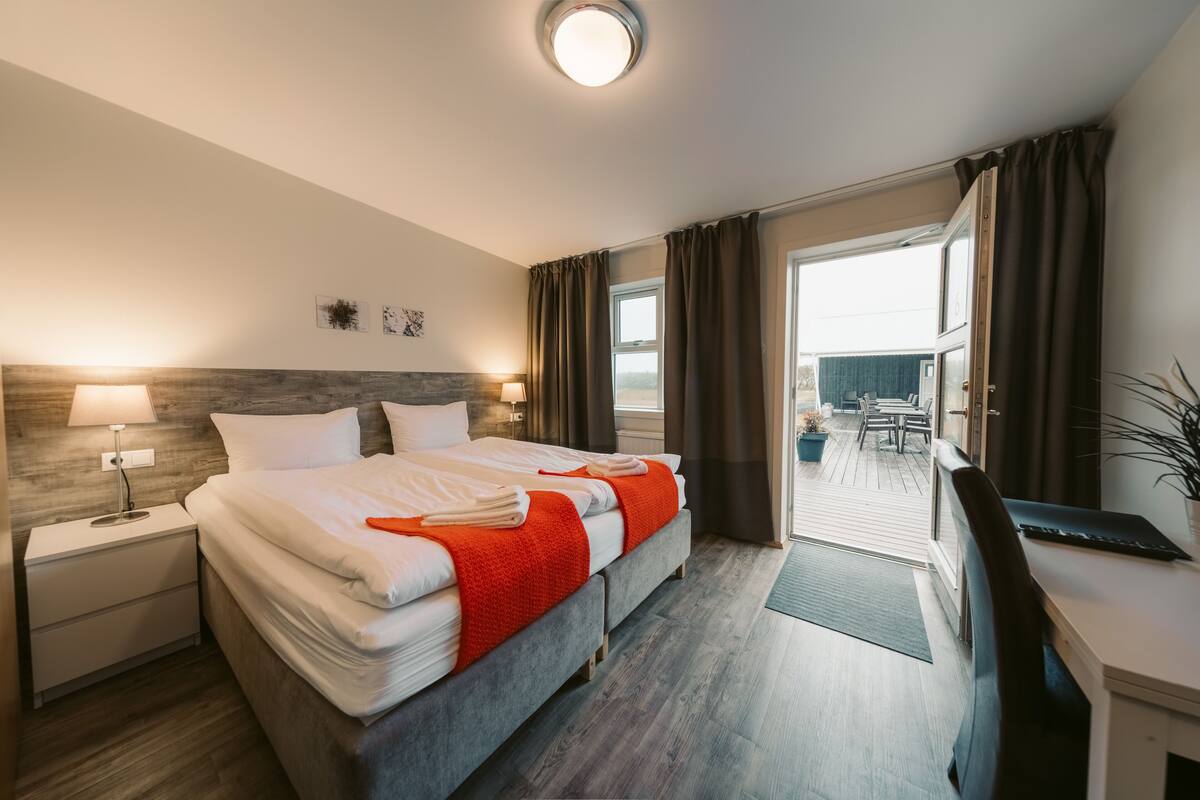 Una habitación de hotel con cama, escritorio, mesita de noche y vistas al exterior.