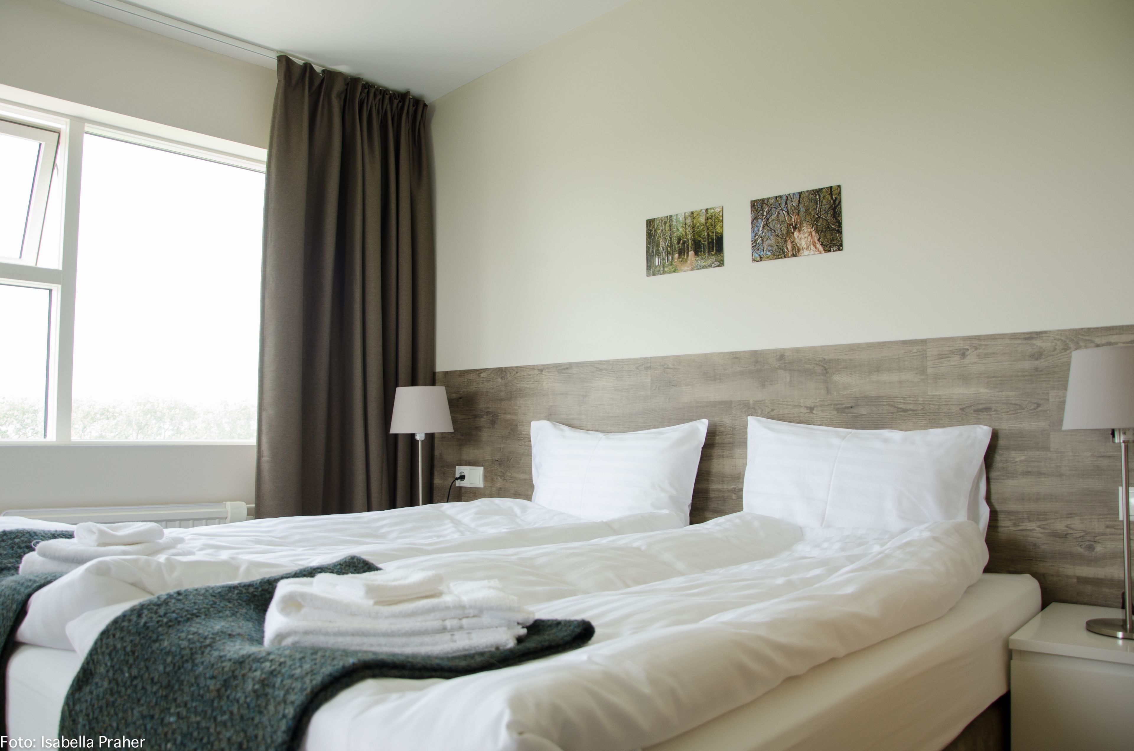 A hotel room with a large bed, two bedside lamps, a window with curtains, and two wall-mounted pictures.