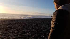A person standing on a rocky beach with waves in the background. - Hotel Vos (Rangarthing ytra)