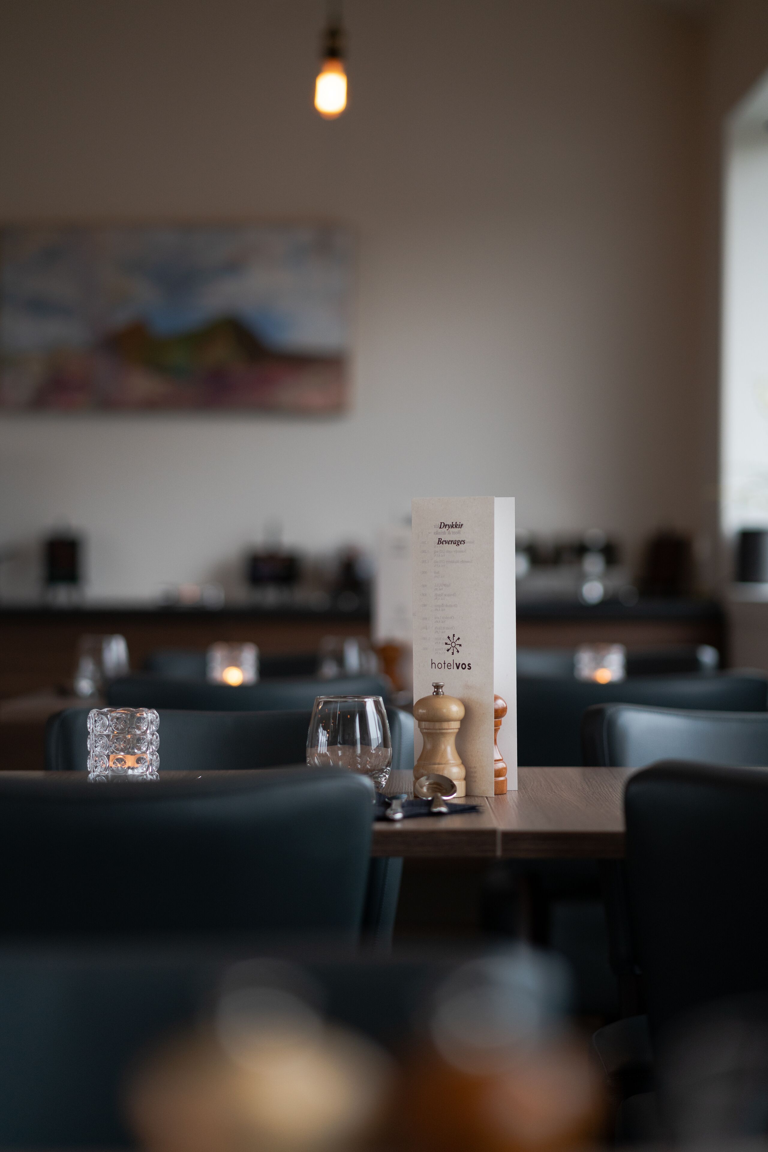 Interior de un restaurante con un menú sobre la mesa, iluminación tenue y un cuadro en la pared.