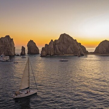 A sailboat on calm waters with rocky formations in the background.