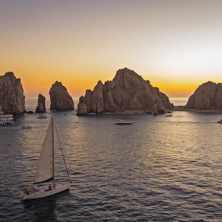 A sailboat on calm waters with rocky formations in the background.