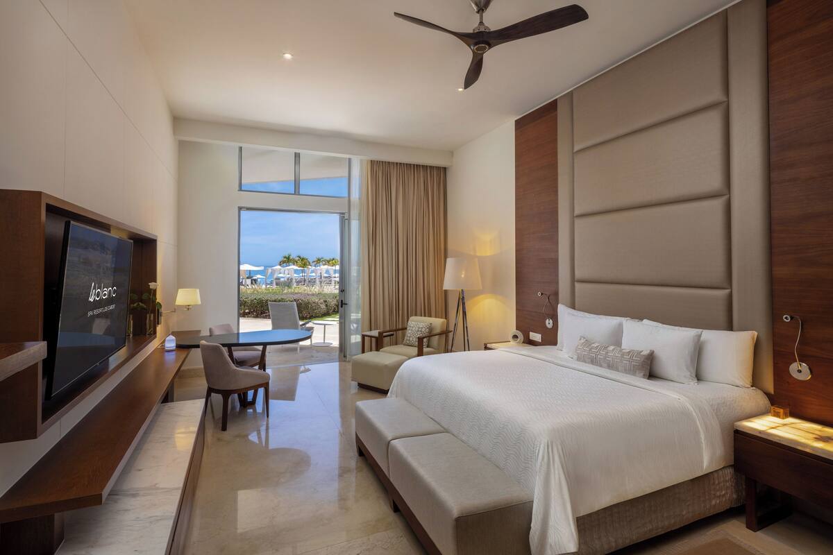 Une chambre d’hôtel moderne dotée d’un grand lit, d’un bureau avec une chaise, d’une télévision et d’un balcon offrant une vue agréable.