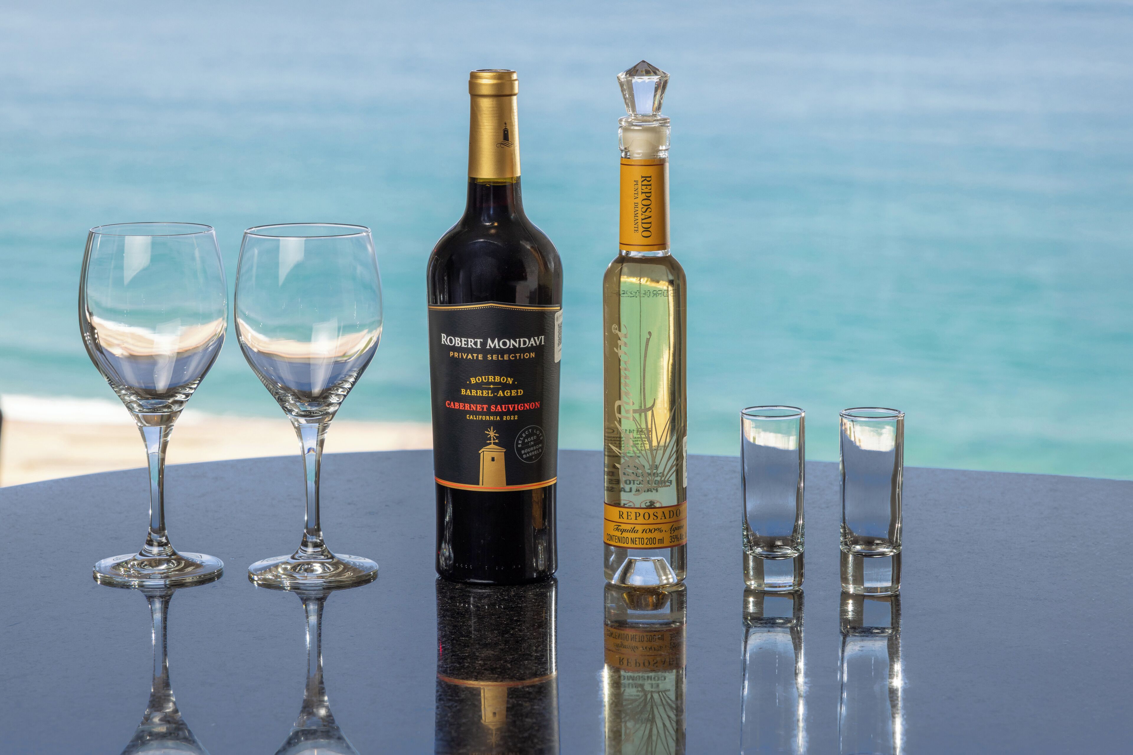 A table with two wine glasses, a bottle of Robert Mondavi Cabernet Sauvignon, and a bottle of Reposado.