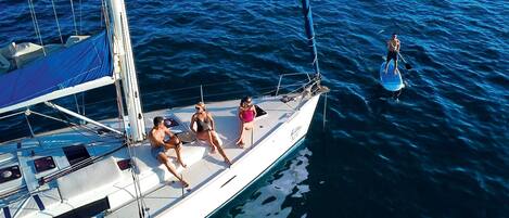 Un velero con tres personas en la cubierta, una persona remando en el agua y una vista despejada del océano.