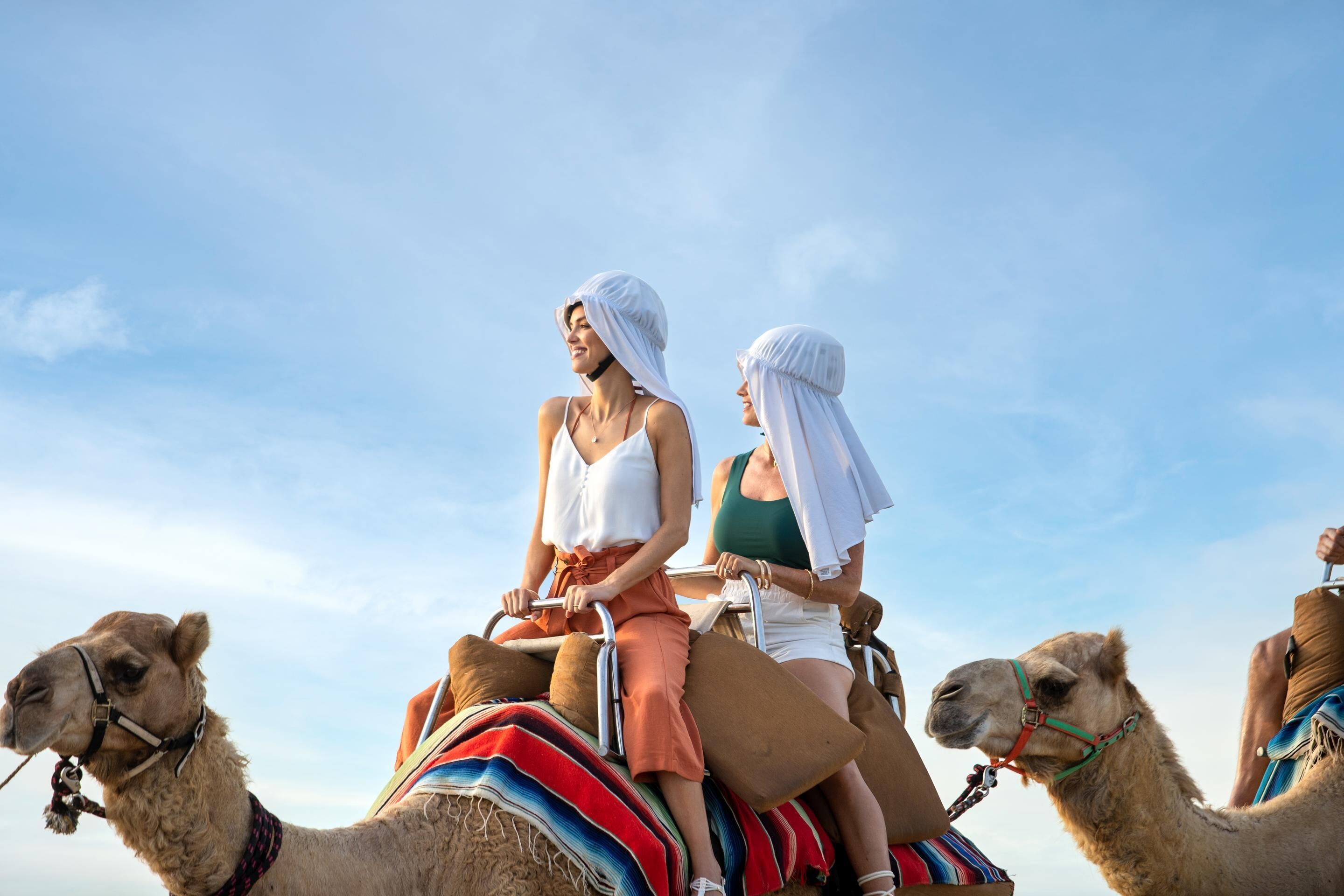 Two people riding camels in a desert setting.