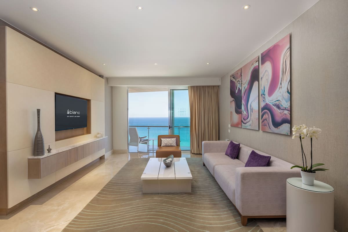 Une chambre d’hôtel moderne dotée d’une grande télévision, d’un canapé, d’une table basse et offrant une vue sur l’océan.