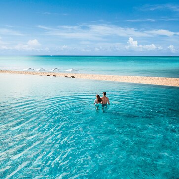 A couple in shallow clear water at a beach with umbrellas and a sandy shore.