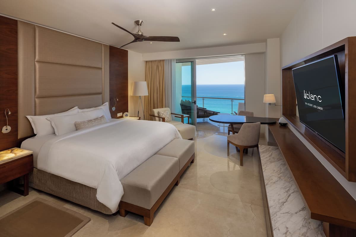 Une chambre d’hôtel avec un grand lit, un bureau avec une chaise, une télévision et un balcon avec vue sur l’océan.
