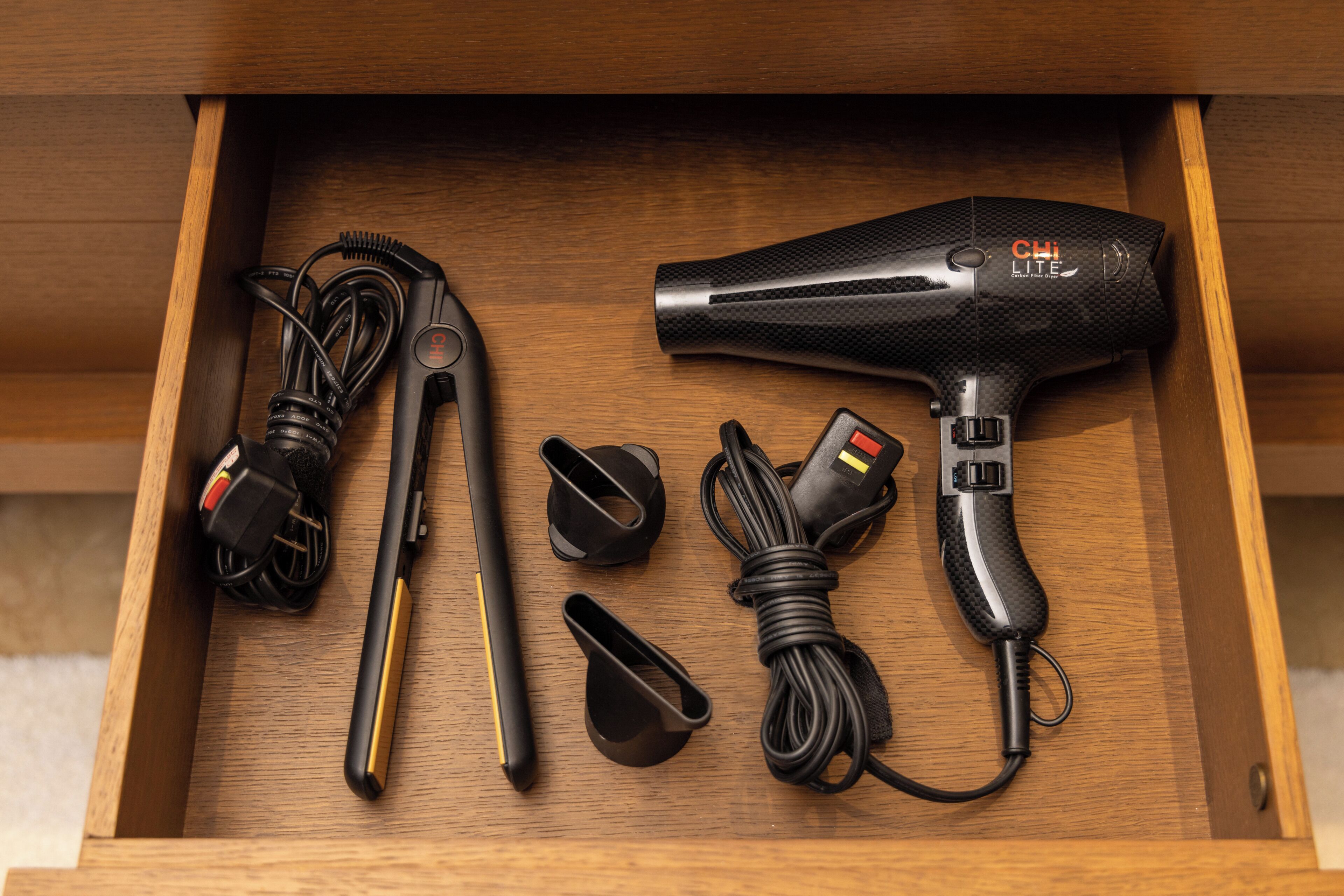A drawer containing a hair dryer, its accessories, and a power cord.