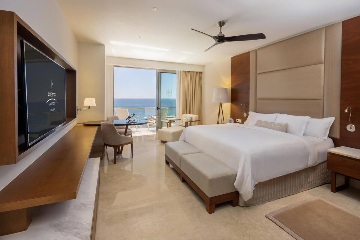 Une chambre d’hôtel moderne dotée d’un grand lit, d’un coin salon avec une table et des chaises, d’une télévision et d’un balcon offrant une vue sur la mer.
