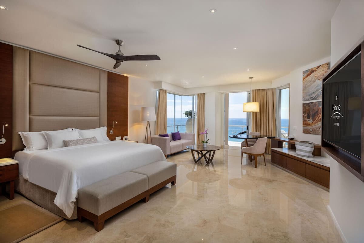 Une chambre d’hôtel avec un grand lit, un ventilateur de plafond, un coin salon avec vue et un téléviseur fixé au mur.