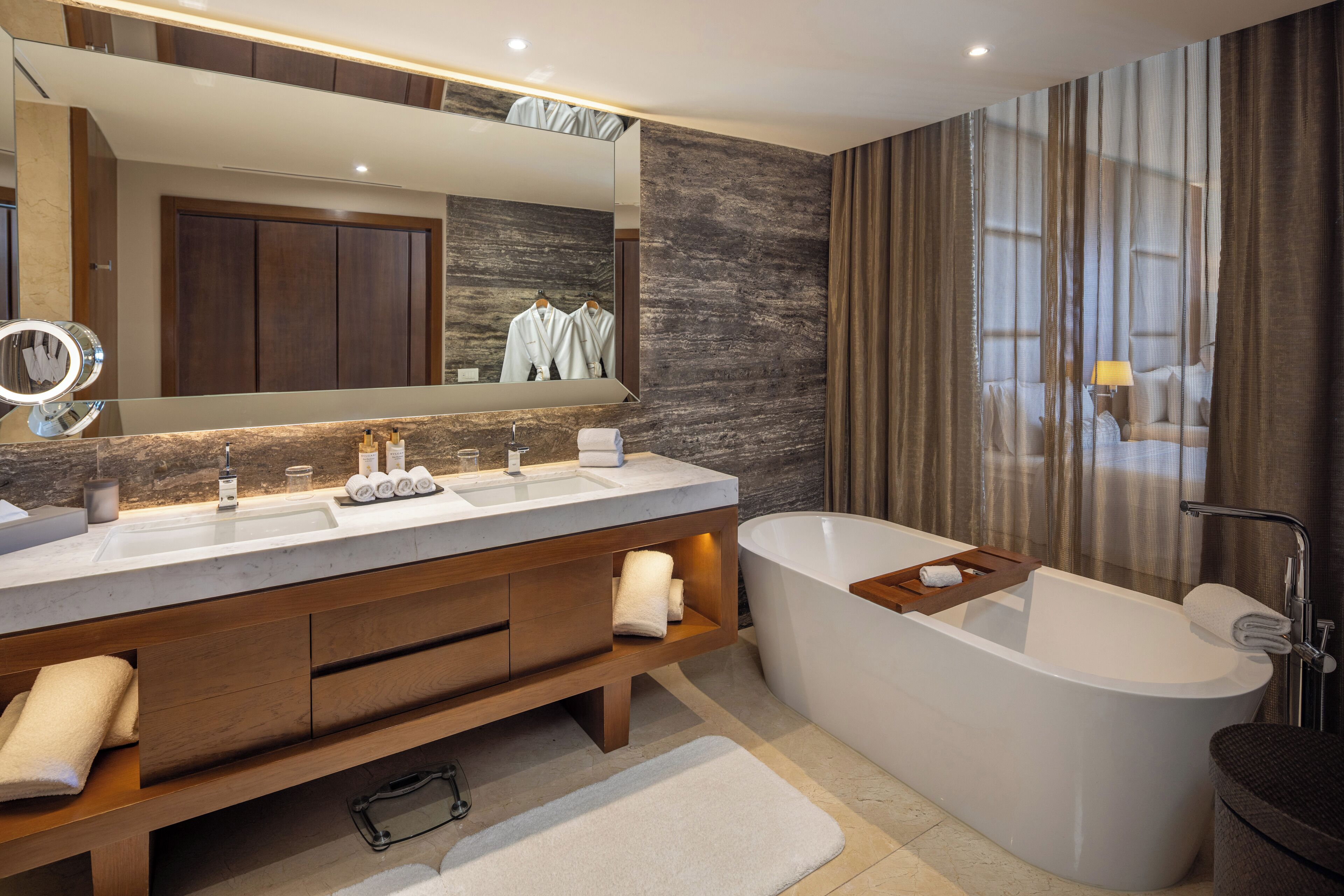 Un baño moderno con una bañera independiente, un espejo grande y un tocador con encimera de mármol.