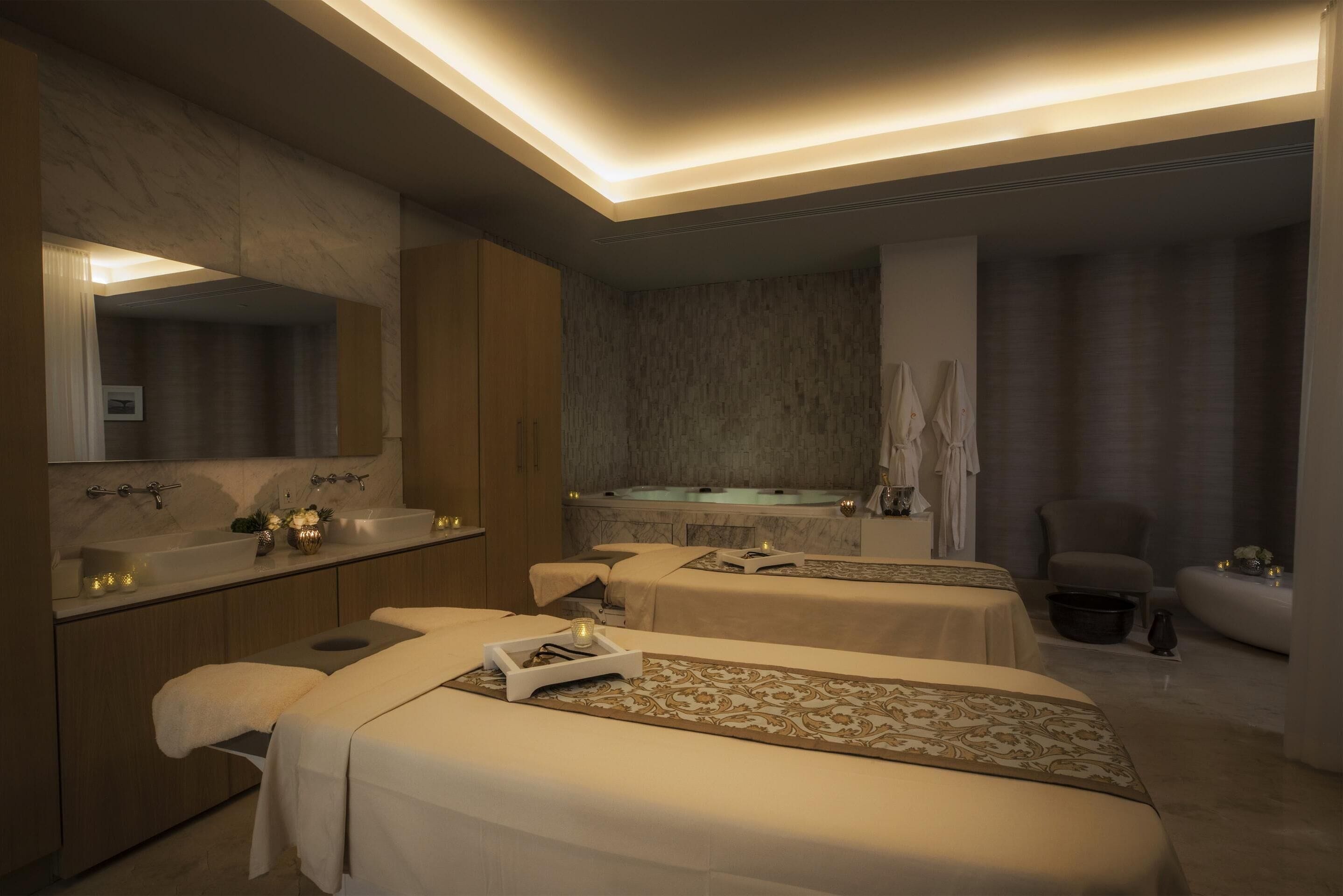 A spa room with two beds, a large mirror, a sink, and a bathtub.
