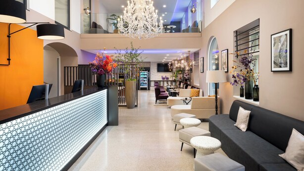 A modern hotel lobby with a reception desk, seating area, chandelier, and artwork. - Leonardo Boutique Hotel Linz City Center (Linz)