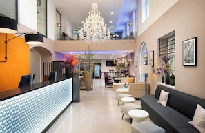 A modern hotel lobby with a reception desk, seating area, chandelier, and artwork.