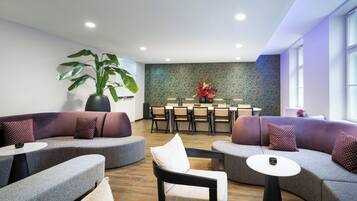 Un área de descanso moderna con un sofá curvo, una mesa de comedor con sillas y una planta grande en maceta.