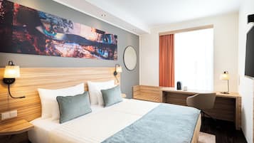 Hotellihuone, jossa on suuri sänky, työpöytä, tuoli, televisio ja taulu seinällä.