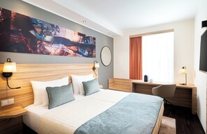 A hotel room with a large bed, a desk, a chair, a TV, and a painting on the wall.