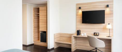 A modern hotel room with a wooden desk, a flat-screen TV, a desk lamp, a chair, and a small coffee table.