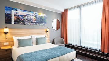 Ein modernes Hotelzimmer mit einem großen Bett, einem Stadtbildgemälde, einem runden Spiegel und Blick ins Freie durch transparente Vorhänge.