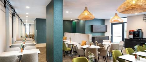 Een modern restaurant met hoge tafels en stoelen, een bar en een in de achtergrond zichtbare keuken.
