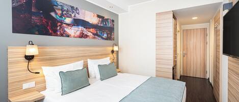 Una habitación de hotel moderna con una cama grande, dos mesitas de noche con lámparas, un cuadro abstracto grande en la pared y un armario de madera.