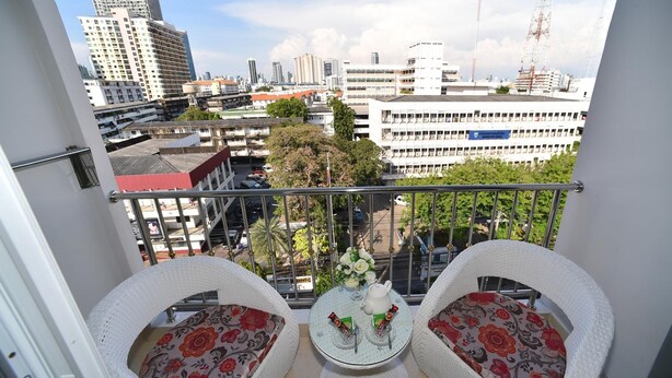 A balcony with two wicker chairs, a small round table with a teapot and two cups, and a view of a cityscape with buildings and trees. - Parvena Hotel (Bangkok)