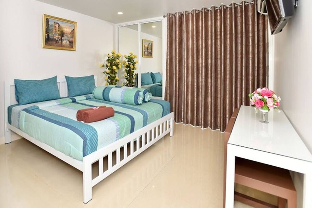 A bedroom with a bed, a desk, a mirror, and curtains.