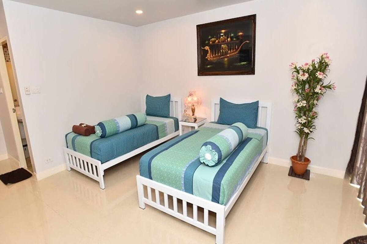 A bedroom with two beds, a nightstand, a potted plant, and a framed picture on the wall.