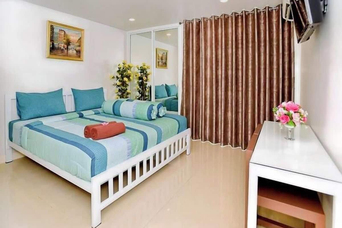 A bedroom with a bed, a desk, a mirror, and a window with curtains.