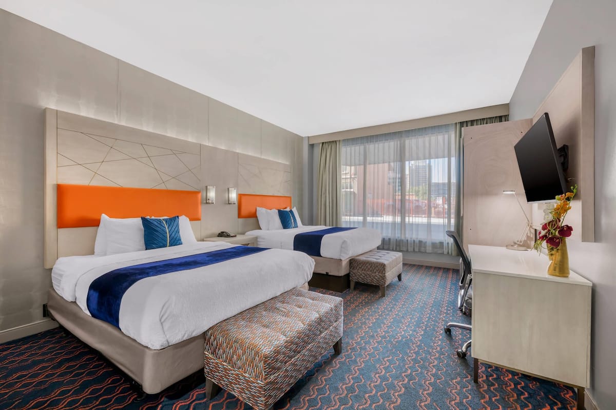Habitación de hotel con dos camas, un escritorio y una televisión.