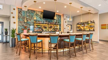 A bar area with a curved counter, multiple bar stools, and a variety of bottles and glasses.