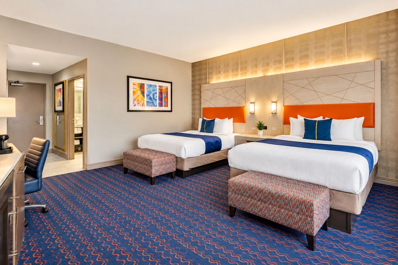 A hotel room with two beds, a desk, and a chair.