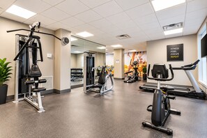 Une salle de sport équipée de machines de cardio, de matériel d’entraînement en force et d’un miroir.
