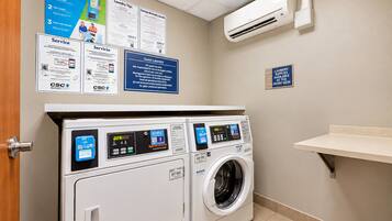 A laundry facility with two front-loading washing machines, a wall-mounted air conditioner, and informational posters.