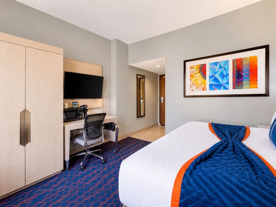 A hotel room with a bed, a desk with a chair, a television, and artwork on the wall.
