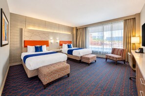 Une chambre d’hôtel avec deux lits, un canapé, une télévision et une grande fenêtre avec des rideaux.