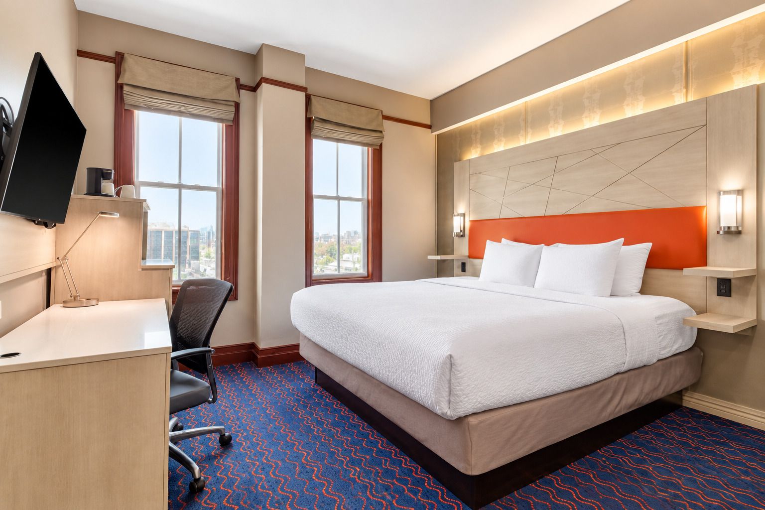 A hotel room with a bed, desk, chair, and a TV.
