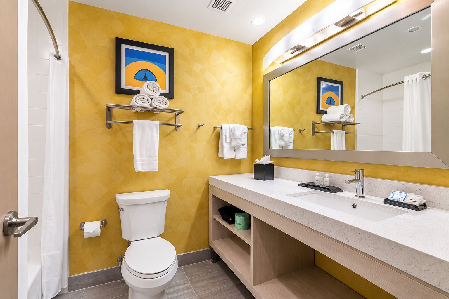A bathroom with a toilet, sink, and mirror. There are towels and a picture on the wall.